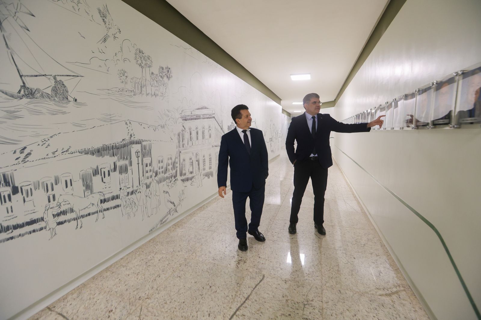 Os deputados Jeová Mota e Leonardo Pinheiro passam pelo galeria onde foram instaladas fotos de todos os parlamentares em exercício